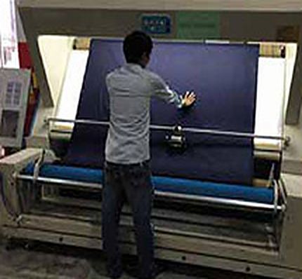 Worker checking denim on a fabric inspection machine