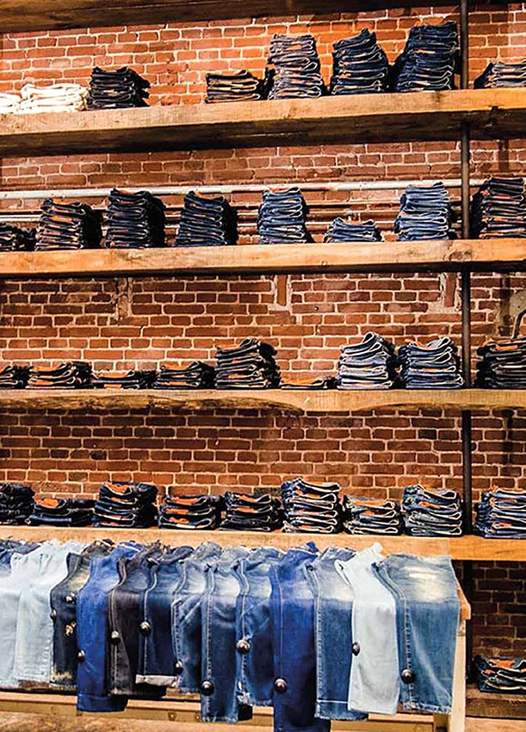 Stacks of folded jeans on wooden shelves against a brick wall